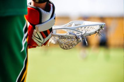A lacrosse player holding his stick and helmet.